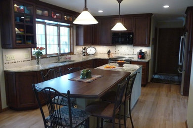 Inspiration for a transitional l-shaped light wood floor eat-in kitchen remodel in Milwaukee with an undermount sink, recessed-panel cabinets, dark wood cabinets, granite countertops, white backsplash, ceramic backsplash, stainless steel appliances and an island
