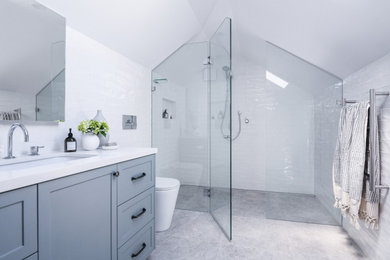 This is an example of a mid-sized traditional master bathroom in Sydney with shaker cabinets, blue cabinets, a two-piece toilet, white tile, subway tile, white walls, porcelain floors, an undermount sink, engineered quartz benchtops, grey floor, a hinged shower door, white benchtops, a niche, a single vanity, a built-in vanity and vaulted.