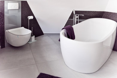 Mittelgroßes Modernes Badezimmer En Suite mit weißen Schränken, freistehender Badewanne, Wandtoilette mit Spülkasten, braunen Fliesen, Mosaikfliesen, grauer Wandfarbe, Betonboden, Aufsatzwaschbecken, Glaswaschbecken/Glaswaschtisch, grauem Boden, grauer Waschtischplatte und schwebendem Waschtisch in Sonstige