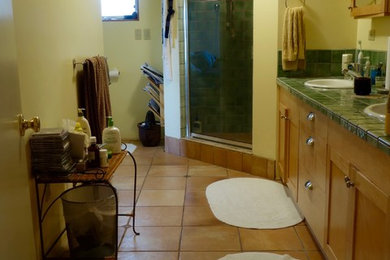 Trendy master ceramic tile ceramic tile corner shower photo in San Francisco with recessed-panel cabinets, light wood cabinets, a drop-in sink and tile countertops