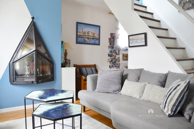 Modelo de sala de estar con biblioteca abierta costera de tamaño medio sin televisor con paredes azules, suelo de madera en tonos medios, chimenea de doble cara y marco de chimenea de metal