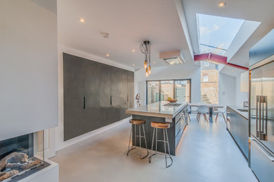 Photo of a medium sized industrial galley open plan kitchen in Surrey with a single-bowl sink, flat-panel cabinets, black cabinets, concrete worktops, metallic splashback, stainless steel appliances, concrete flooring and an island.