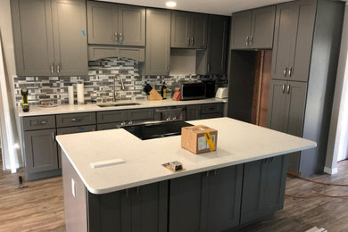 Example of a minimalist vinyl floor kitchen design in Tampa with gray cabinets, an island and white countertops
