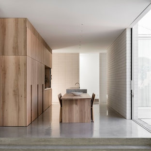 Foto de cocina comedor minimalista con armarios con paneles lisos, puertas de armario de madera clara, suelo de cemento, una isla y suelo gris