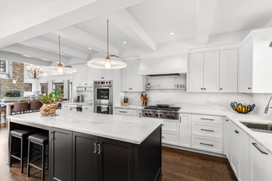 Transitional l-shaped dark wood floor, brown floor and exposed beam kitchen photo in Minneapolis with an undermount sink, shaker cabinets, white cabinets, white backsplash, stone slab backsplash, stainless steel appliances, an island and white countertops