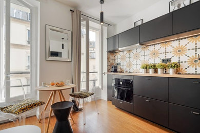 Idée de décoration pour une cuisine ouverte linéaire design de taille moyenne avec un placard à porte affleurante, des portes de placard noires, un plan de travail en bois, une crédence jaune, une crédence en carreau de ciment, un électroménager noir, parquet clair, aucun îlot, un sol marron et un plan de travail marron.