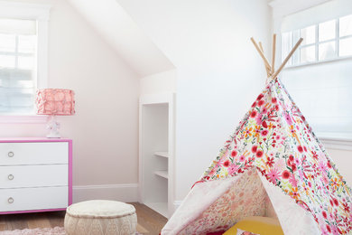 This is an example of a beach style kids' bedroom for kids 4-10 years old and girls in New York with white walls, medium hardwood floors and beige floor.