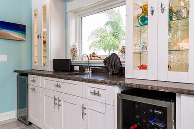 Photo of a medium sized beach style galley wet bar in Tampa with a submerged sink, shaker cabinets, white cabinets, granite worktops, brown splashback, marble splashback, beige floors and light hardwood flooring.