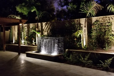 Patio - large tropical backyard concrete paver patio idea in Orange County with a pergola