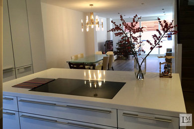Photo of a contemporary eat-in kitchen in London with flat-panel cabinets, white cabinets, marble benchtops, black appliances, dark hardwood floors and with island.