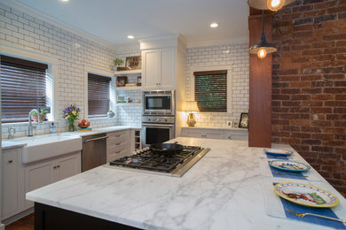 Mid-sized country u-shaped dark wood floor and brown floor eat-in kitchen photo in Other with a farmhouse sink, shaker cabinets, white cabinets, marble countertops, white backsplash, subway tile backsplash, stainless steel appliances and an island