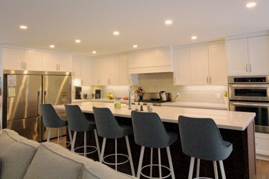 Open concept kitchen - large coastal l-shaped porcelain tile and brown floor open concept kitchen idea in Other with a double-bowl sink, shaker cabinets, white cabinets, quartz countertops, white backsplash, ceramic backsplash, stainless steel appliances, an island and white countertops