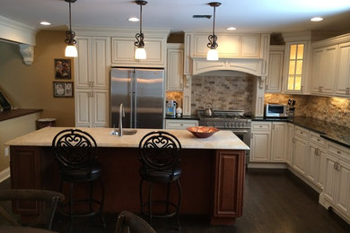 Example of a mid-sized classic u-shaped dark wood floor and brown floor kitchen design in New York with a drop-in sink, raised-panel cabinets, white cabinets, granite countertops, beige backsplash, stone tile backsplash, stainless steel appliances and an island