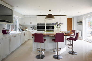 This is an example of a mid-sized transitional kitchen in Hertfordshire with a double-bowl sink, shaker cabinets, white cabinets, stainless steel appliances and with island.