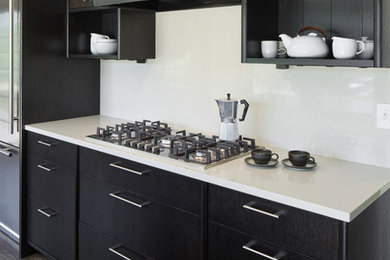 1950s l-shaped medium tone wood floor and brown floor enclosed kitchen photo in Portland with an undermount sink, flat-panel cabinets, dark wood cabinets, quartz countertops, white backsplash, stone slab backsplash, stainless steel appliances and an island
