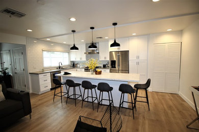Photo of a mid-sized contemporary l-shaped open plan kitchen in Los Angeles with an undermount sink, shaker cabinets, white cabinets, quartzite benchtops, white splashback, subway tile splashback, stainless steel appliances, light hardwood floors, with island, beige floor and white benchtop.