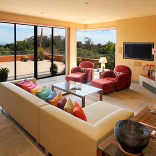 Diseño de salón para visitas abierto, mediterráneo, grande, con paredes amarillas, suelo de baldosas de cerámica, chimenea tradicional, marco de chimenea de metal, televisor colgado en la pared y suelo gris