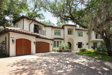 Large tuscan beige two-story stucco house exterior photo in Tampa with a hip roof and a tile roof