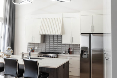 Large trendy l-shaped light wood floor, brown floor and tray ceiling eat-in kitchen photo in Calgary with an undermount sink, flat-panel cabinets, white cabinets, quartzite countertops, gray backsplash, ceramic backsplash, stainless steel appliances, an island and white countertops