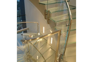 На фото: большая изогнутая лестница в стиле модернизм с стеклянными ступенями и стеклянными подступенками с