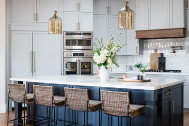 Eat-in kitchen - mid-sized coastal medium tone wood floor and brown floor eat-in kitchen idea in Phoenix with a farmhouse sink, recessed-panel cabinets, blue cabinets, marble countertops, white backsplash, stone tile backsplash, paneled appliances, an island and white countertops