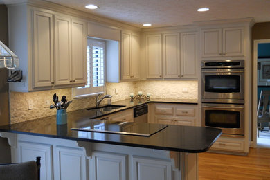 Inspiration for a mid-sized contemporary l-shaped medium tone wood floor eat-in kitchen remodel in Atlanta with a drop-in sink, raised-panel cabinets, white cabinets, granite countertops, beige backsplash, stone tile backsplash, stainless steel appliances and no island