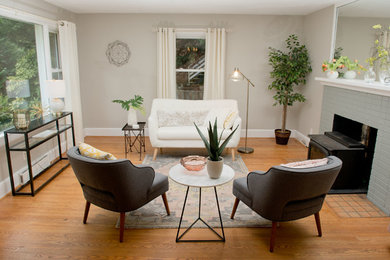 Example of a small trendy enclosed light wood floor and beige floor living room design in Other with gray walls, a wood stove, a brick fireplace and no tv