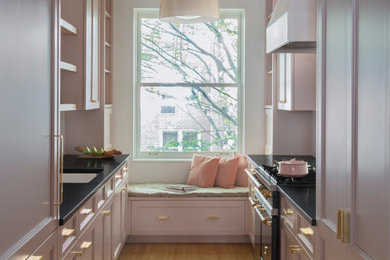 Photo of a small traditional galley separate kitchen in New York with an undermount sink, shaker cabinets, pink cabinets, granite benchtops, white splashback, ceramic splashback, panelled appliances, light hardwood floors, no island, beige floor and black benchtop.