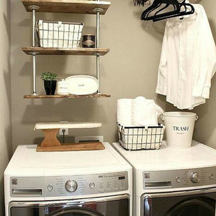 This is an example of a small industrial laundry cupboard in Tampa with beige walls and a side by side washer and dryer.
