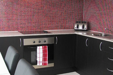 メルボルンにあるモダンスタイルのおしゃれなキッチン (シングルシンク、赤いキッチンパネル、ガラス板のキッチンパネル、磁器タイルの床) の写真