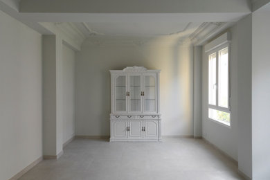 Imagen de biblioteca en casa cerrada y beige y blanca tradicional renovada grande con paredes blancas, suelo de baldosas de porcelana, televisor colgado en la pared, suelo beige y vigas vistas