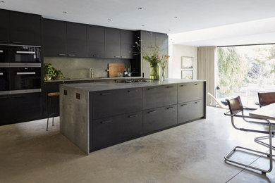 Inspiration for a large contemporary galley eat-in kitchen in Sussex with flat-panel cabinets, concrete benchtops, grey splashback, stone slab splashback, black appliances, concrete floors, with island, grey floor, grey benchtop, an undermount sink and black cabinets.