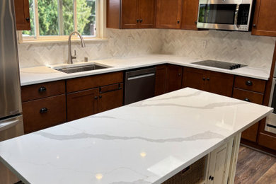 Inspiration for a mid-sized timeless l-shaped eat-in kitchen remodel in Seattle with an undermount sink, shaker cabinets, brown cabinets, quartzite countertops, white backsplash, stone tile backsplash, stainless steel appliances, an island and white countertops