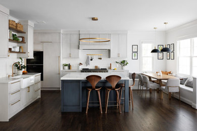 Example of a mid-sized transitional u-shaped dark wood floor and brown floor eat-in kitchen design in DC Metro with a farmhouse sink, shaker cabinets, gray cabinets, white backsplash, black appliances, an island and white countertops
