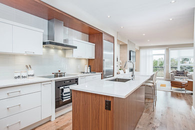 Inspiration for a mid-sized modern single-wall open plan kitchen in Toronto with an undermount sink, flat-panel cabinets, white cabinets, marble benchtops, white splashback, ceramic splashback, stainless steel appliances, light hardwood floors and with island.