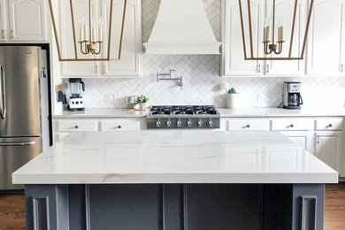 This is an example of a large country single-wall kitchen in Raleigh with raised-panel cabinets, white cabinets, marble benchtops, white splashback, subway tile splashback, stainless steel appliances, medium hardwood floors, with island, brown floor and white benchtop.
