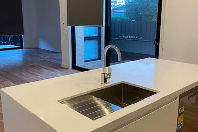 Photo of a small contemporary galley kitchen pantry in Melbourne with an undermount sink, flat-panel cabinets, white cabinets, quartz benchtops, mirror splashback, stainless steel appliances, medium hardwood floors, with island and white benchtop.
