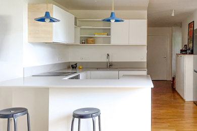 Idées déco pour une cuisine ouverte encastrable et beige et blanche contemporaine en U de taille moyenne avec un évier encastré, un placard à porte plane, des portes de placard blanches, un plan de travail en surface solide, une crédence grise, parquet clair, îlot, un sol beige, un plan de travail gris et un plafond décaissé.