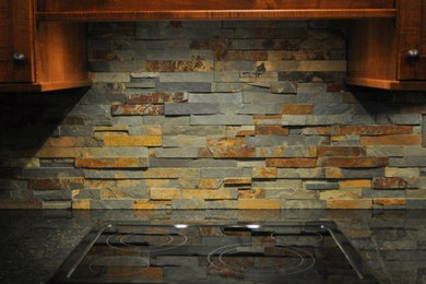 Example of a mid-sized southwest kitchen design in Cleveland with dark wood cabinets, multicolored backsplash, stone tile backsplash and black appliances