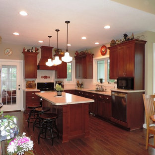 На фото: п-образная кухня среднего размера в классическом стиле с фасадами в стиле шейкер, фасадами цвета дерева среднего тона, техникой из нержавеющей стали, островом, коричневым полом, кладовкой, бежевой столешницей и темным паркетным полом с