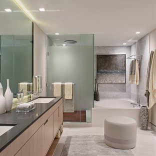 Bathroom - contemporary gray tile beige floor bathroom idea in Miami with flat-panel cabinets, light wood cabinets, beige walls, an undermount sink, a hinged shower door and black countertops