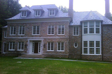 Inspiration for a large timeless gray two-story stone house exterior remodel in New York with a hip roof and a shingle roof