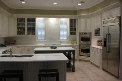 Example of a mid-sized classic u-shaped porcelain tile kitchen design in Jacksonville with an undermount sink, raised-panel cabinets, white cabinets, marble countertops, white backsplash, ceramic backsplash and stainless steel appliances