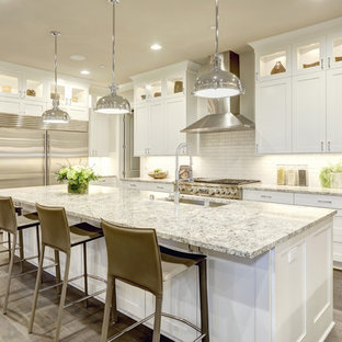 Photo of a large traditional l-shaped kitchen/diner in New York with a submerged sink, shaker cabinets, white cabinets, white splashback, metro tiled splashback, stainless steel appliances, light hardwood flooring, an island and granite worktops.