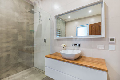 This is an example of a mid-sized contemporary master bathroom in Sydney with furniture-like cabinets, a freestanding tub, an open shower, a two-piece toilet, multi-coloured tile, multi-coloured walls, porcelain floors, a vessel sink, wood benchtops, grey floor and an open shower.