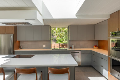 Large 1960s l-shaped porcelain tile, gray floor and wood ceiling open concept kitchen photo in San Francisco with an undermount sink, flat-panel cabinets, medium tone wood cabinets, quartz countertops, gray backsplash, porcelain backsplash, stainless steel appliances, an island and white countertops