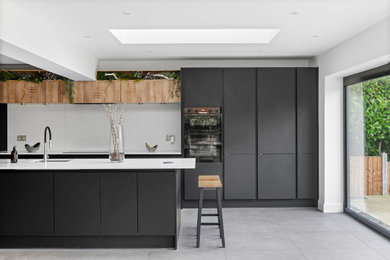 Inspiration for a contemporary galley kitchen in Essex with a submerged sink, flat-panel cabinets, grey cabinets, white splashback, stainless steel appliances, an island, grey floors and white worktops.