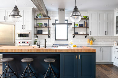 Exemple d'une grande cuisine américaine chic en U avec un évier de ferme, un placard à porte shaker, des portes de placard grises, un plan de travail en bois, une crédence blanche, une crédence en carreau de porcelaine, un électroménager en acier inoxydable, parquet foncé, îlot, un sol marron et un plan de travail blanc.