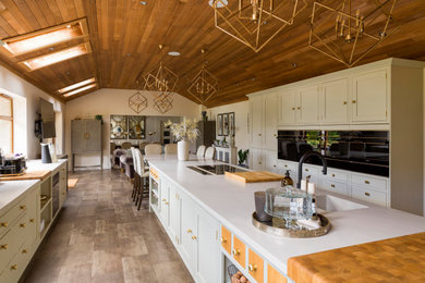 Large farmhouse open plan kitchen in Other with an integrated sink, shaker cabinets, an island, grey worktops and a vaulted ceiling.