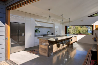 Photo of a large beach style galley open plan kitchen in Sydney with a drop-in sink, flat-panel cabinets, white cabinets, concrete benchtops, white splashback, subway tile splashback, stainless steel appliances, concrete floors, with island, grey floor and grey benchtop.